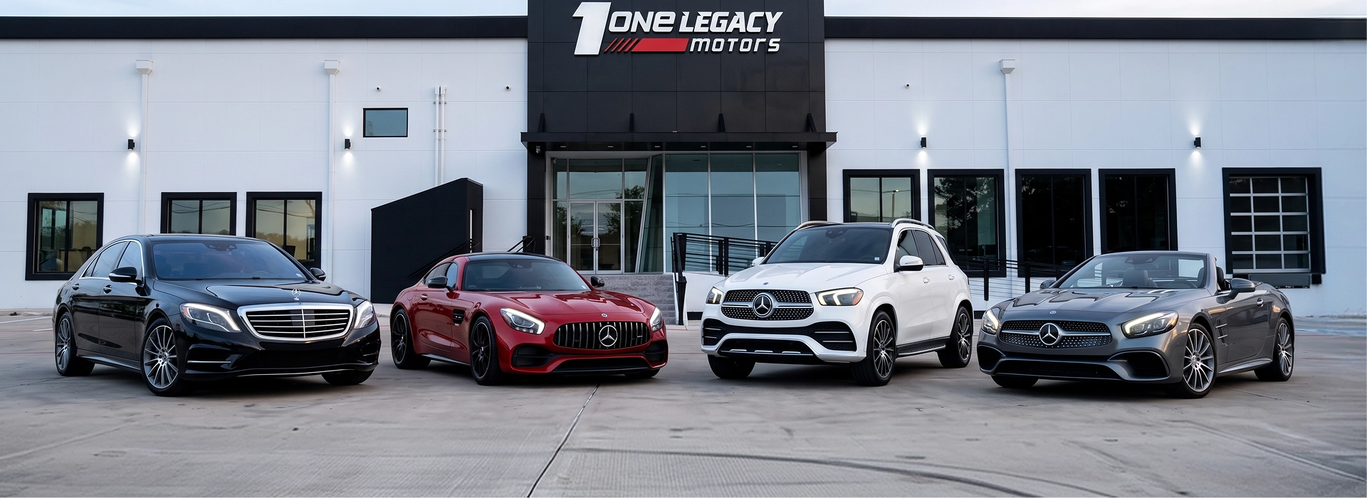 A black S-Class, a red AMG GT, a white GLS and a grey SL parked in a row outside the One Legacy Motors showroom in Carrollton, Texas