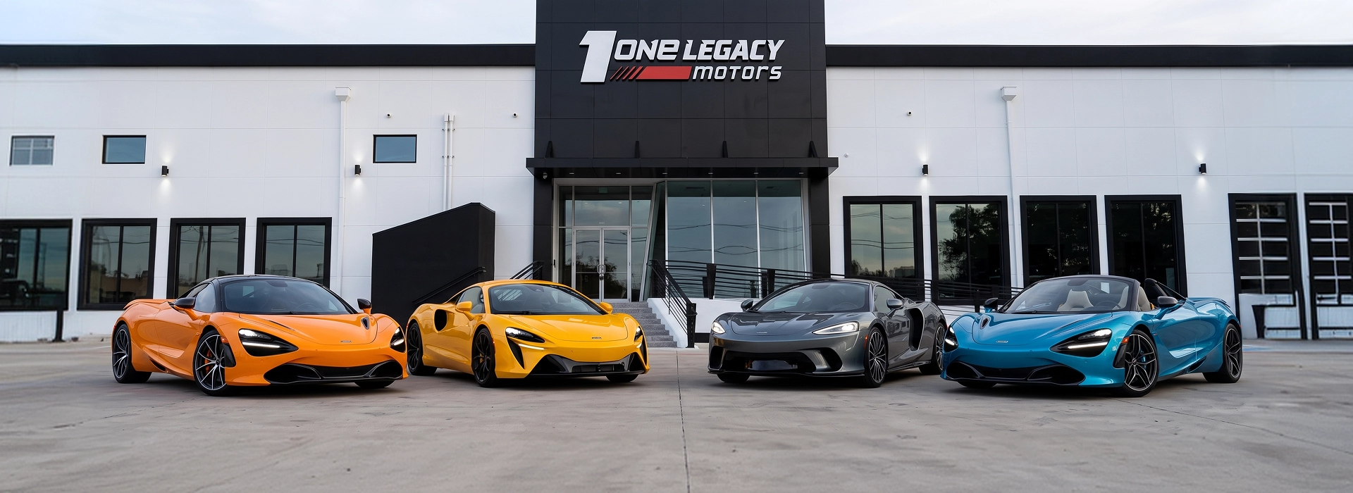 An orange McLaren 720S, a yellow Artura, a grey GT and a blue 720S Spider parked in a row outside the One Legacy Motors showroom in Carrollton, Texas