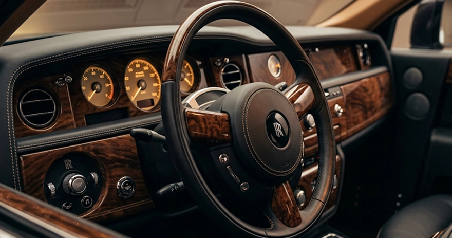 Rolls-Royce cockpit with a burr-wood dashboard, chrome-ringed dials and a leather steering wheel carrying the RR monogram