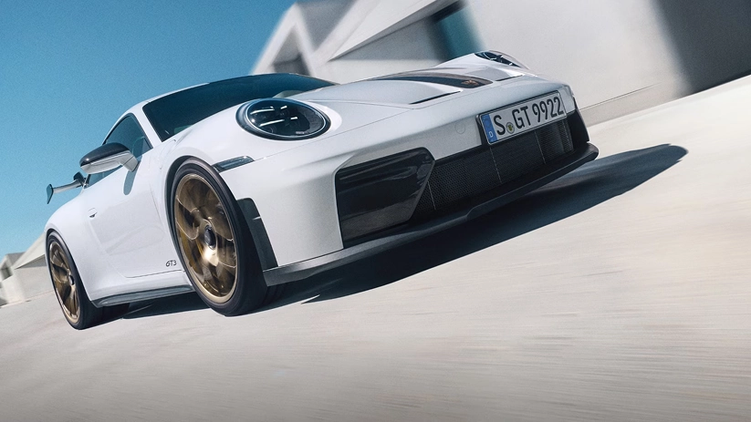 White Porsche 911 GT3 on gold wheels cornering hard past a white building