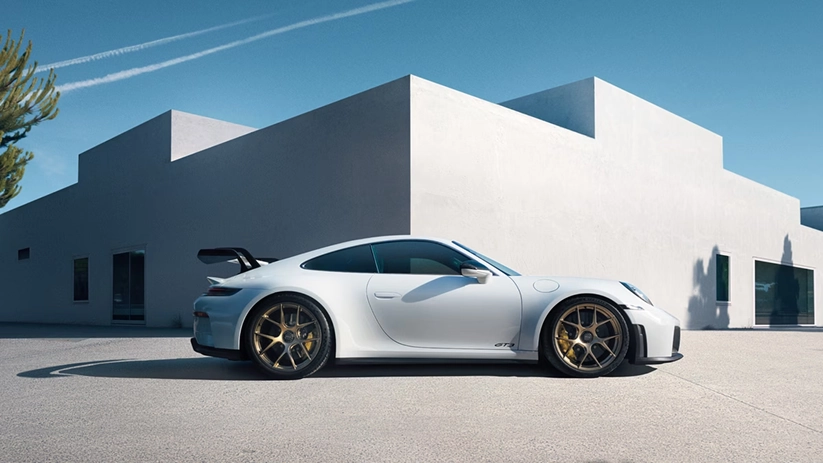 White Porsche 911 GT3 in profile beside a white cubic building under a clear blue sky