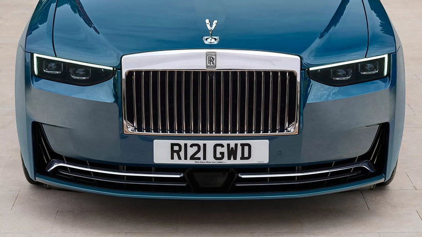 Head-on view of a blue Rolls-Royce Ghost showing its illuminated Pantheon grille and the Spirit of Ecstasy