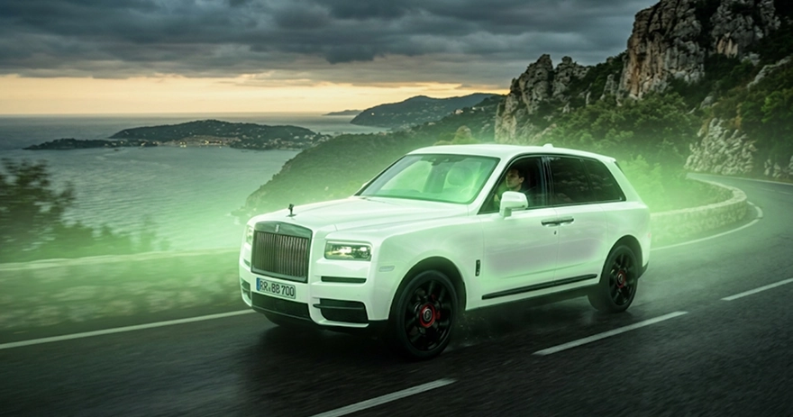 White Rolls-Royce Cullinan Black Badge sweeping along a coastal mountain road under a stormy sky