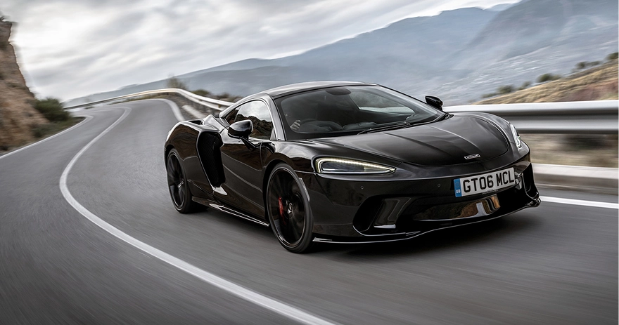 Black McLaren GT on a sweeping mountain road, seen from the front three-quarter