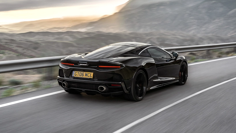 Black McLaren GT driving away along a coastal mountain road