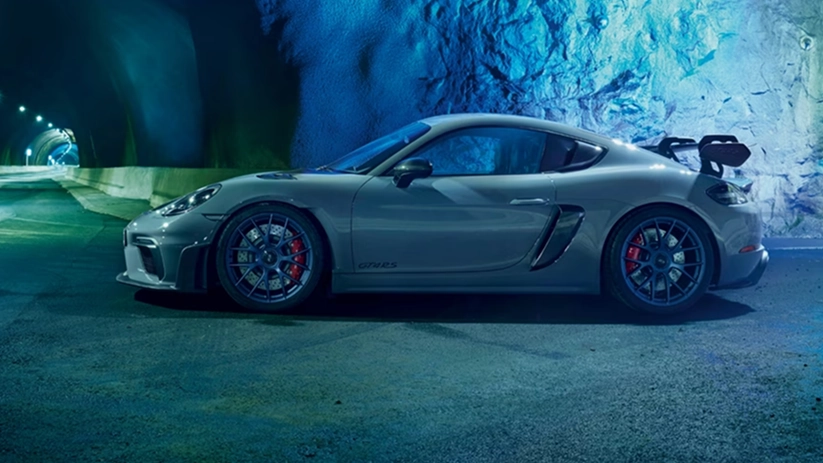 Grey Porsche 718 Cayman GT4 RS in profile in front of a floodlit blue rock wall