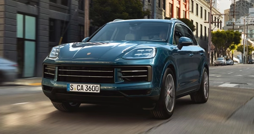 Teal Porsche Cayenne driving down a sunlit city street