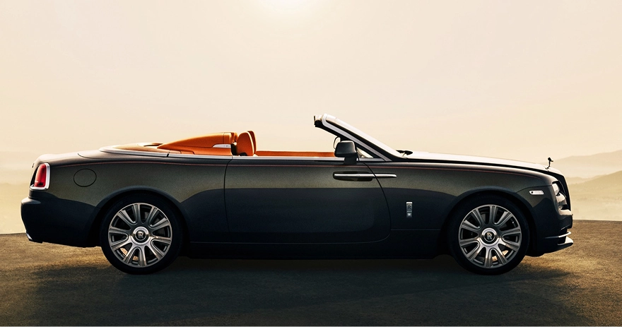 Dark Rolls-Royce Dawn convertible in profile with the roof down and an orange leather interior