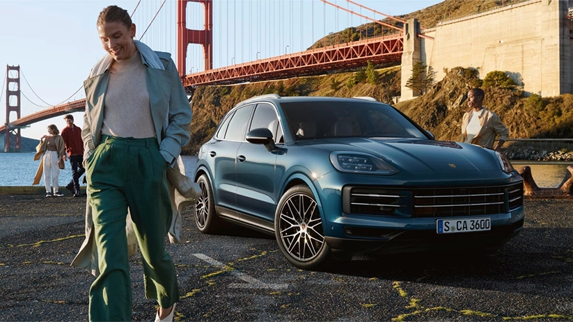 A woman walking away from a teal Porsche Cayenne parked near the Golden Gate Bridge