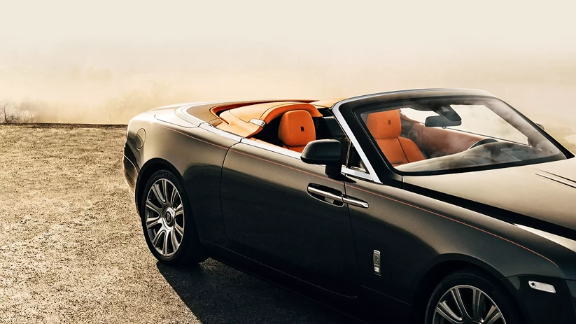 Silver-brown Rolls-Royce Dawn parked on desert sand with its orange interior on show
