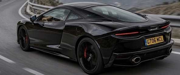 Rear three-quarter of a black McLaren GT with its tail lights lit, on a mountain road