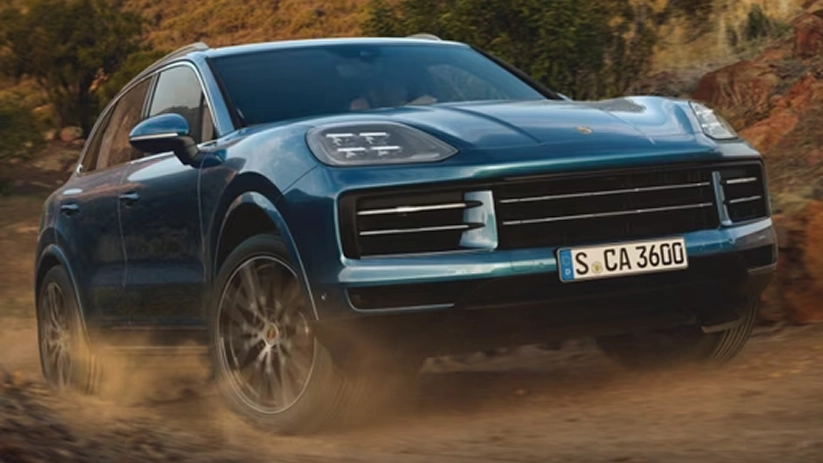 Teal Porsche Cayenne kicking up dust on a dirt trail