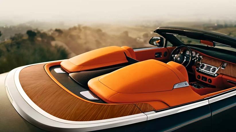 Overhead view of a Rolls-Royce Dawn's orange rear seats under the polished wood tonneau cover