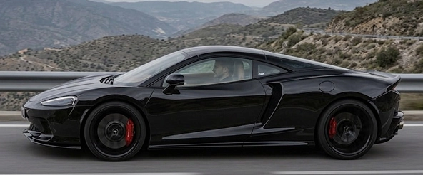 Black McLaren GT in profile on a mountain road, showing its long grand touring silhouette