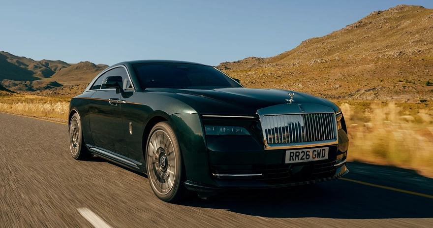 Dark green Rolls-Royce Spectre at speed on an open road below dry hills