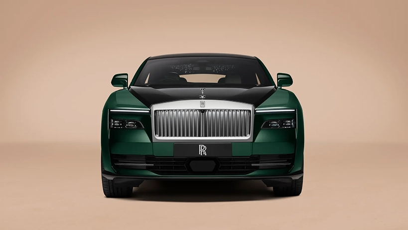Head-on view of a dark green Rolls-Royce Spectre showing its split headlamps and illuminated grille