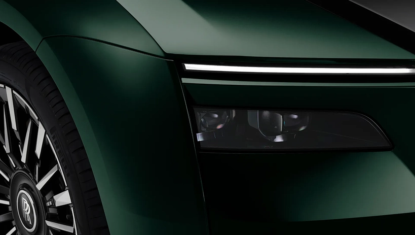 Close-up of a dark green Rolls-Royce Spectre's headlight, wing and polished wheel