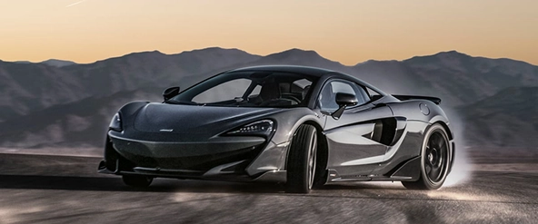 Grey McLaren 600LT sliding through a corner at sunset, seen from the front three-quarter
