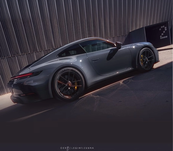 Grey Porsche 911 GT3 seen from the rear three-quarter beside a corrugated metal wall at sunset