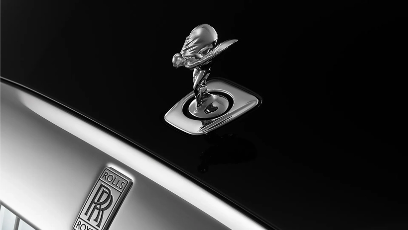 The Spirit of Ecstasy figurine standing on the polished black bonnet of a Rolls-Royce above the Rolls-Royce badge