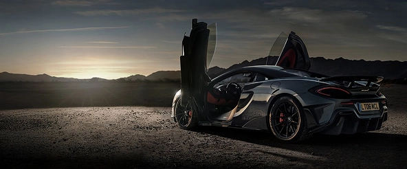Grey McLaren 600LT with both dihedral doors raised, parked in the desert at dusk