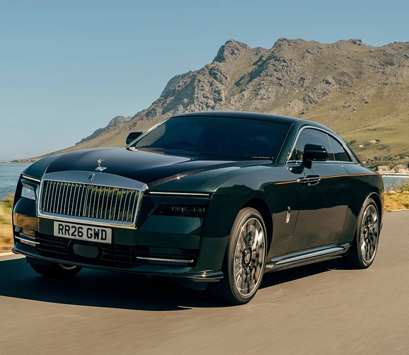 Dark green Rolls-Royce Spectre driving a coastal road below a rocky headland