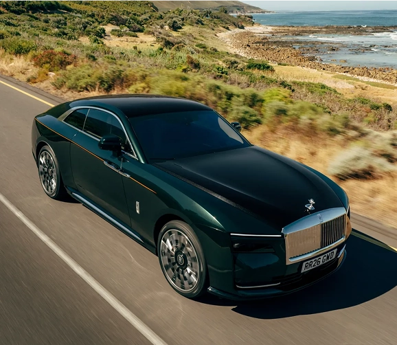 Dark green Rolls-Royce Spectre seen from above on a road beside the sea