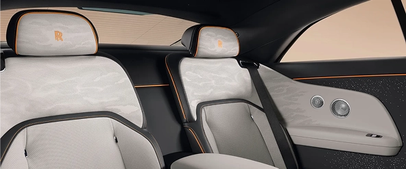 Rear cabin of a Rolls-Royce Spectre in pale grey and black leather with orange piping