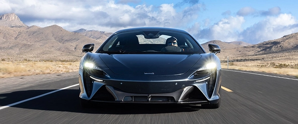 Grey McLaren Artura driving head-on along a desert road with mountains behind