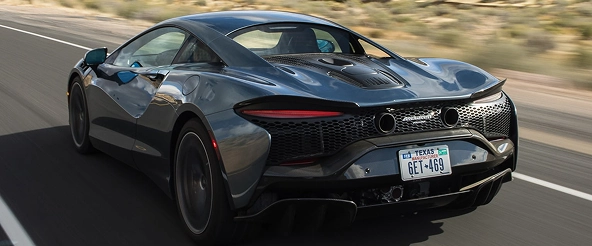 Rear three-quarter of a grey McLaren Artura on a highway, showing its diffuser and exhausts