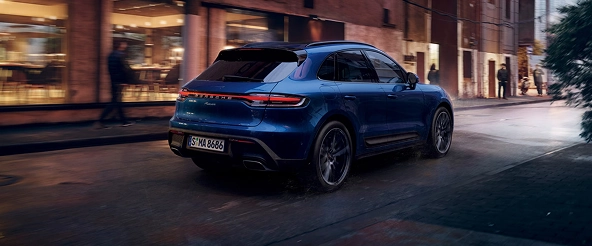 Blue Porsche Macan seen from the rear on a wet city street at night