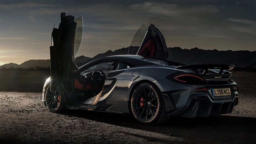 Grey McLaren 600LT with both dihedral doors raised, parked in the desert at dusk
