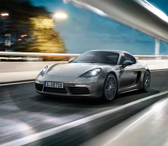 Silver Porsche 718 Cayman at speed on a city road at night with the lights streaking past