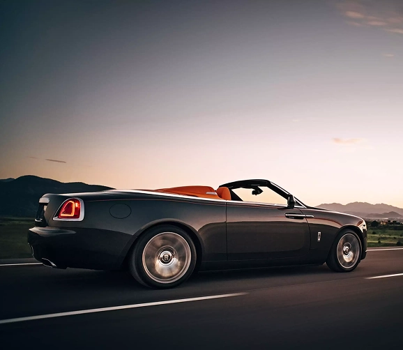 Dark Rolls-Royce Dawn convertible at speed at dusk with the roof down