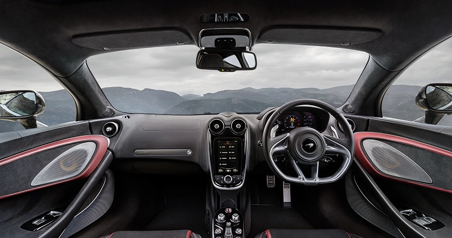 McLaren GT cabin seen from behind the seats, with red-trimmed door cards and mountains through the windscreen