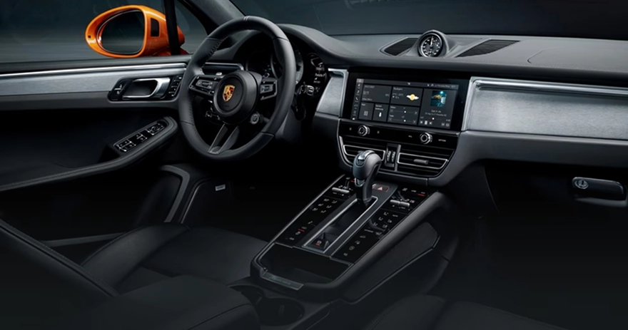 Porsche Macan cockpit with its centre touchscreen, console switchgear and an orange wing mirror in view