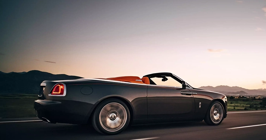 Dark Rolls-Royce Dawn convertible at speed at dusk with its taillights lit