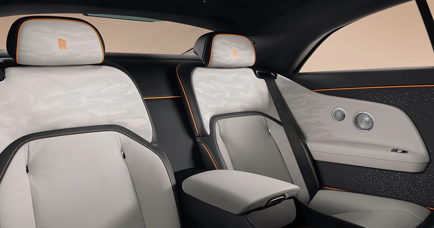 Rear cabin of a Rolls-Royce Spectre in pale grey leather with orange piping and a starlight door panel