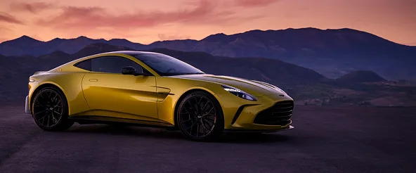 Yellow Aston Martin Vantage parked against a mountain range at dusk