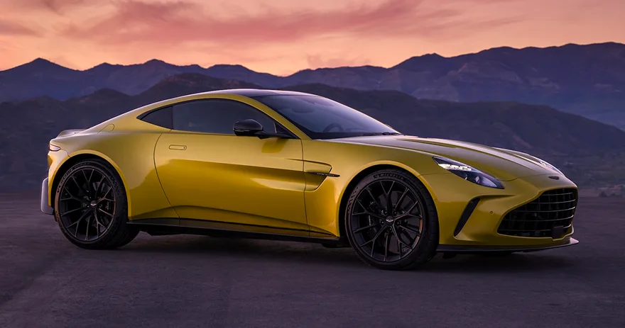 Yellow Aston Martin Vantage parked against a mountain backdrop at dusk