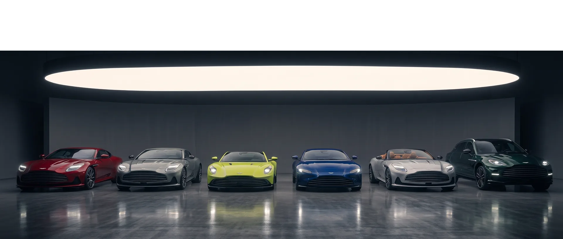 Six Aston Martins in red, grey, green, blue, silver and dark green lined up beneath a showroom light