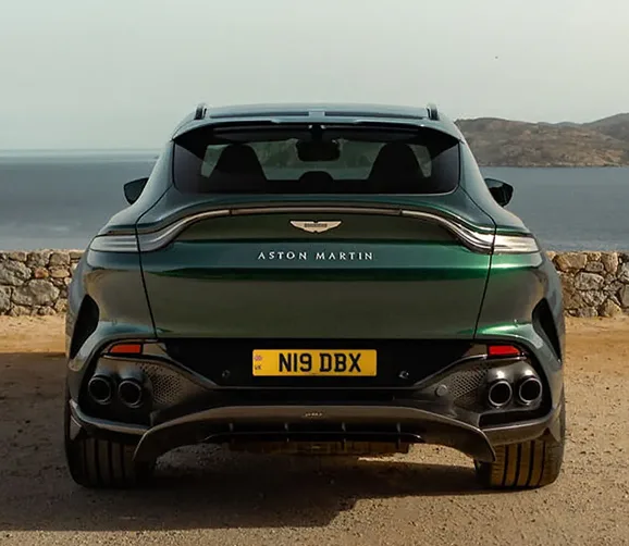 Green Aston Martin DBX 707 parked on a coastal road, seen from behind