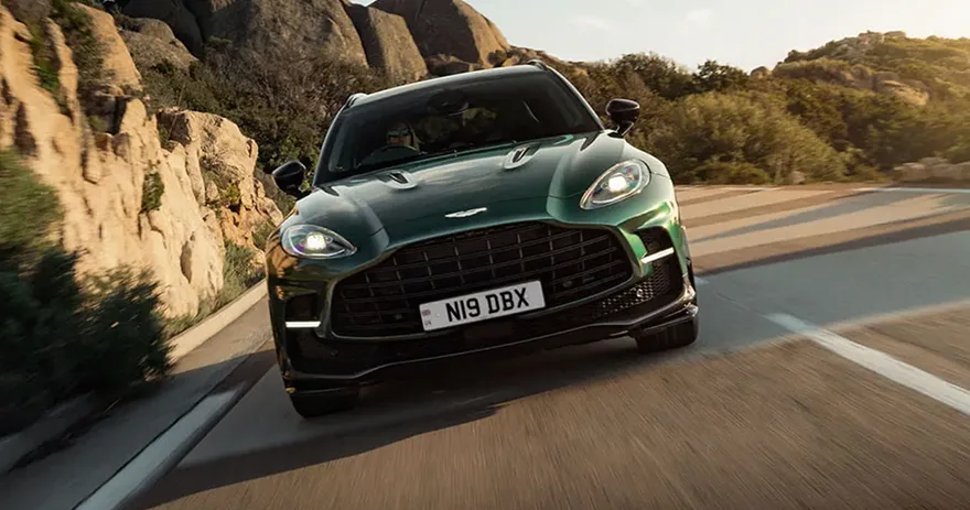 Dark green Aston Martin DBX 707 driving along a coastal mountain road at sunset