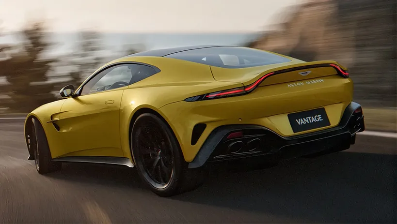 Rear three-quarter view of a yellow Aston Martin Vantage on a mountain road