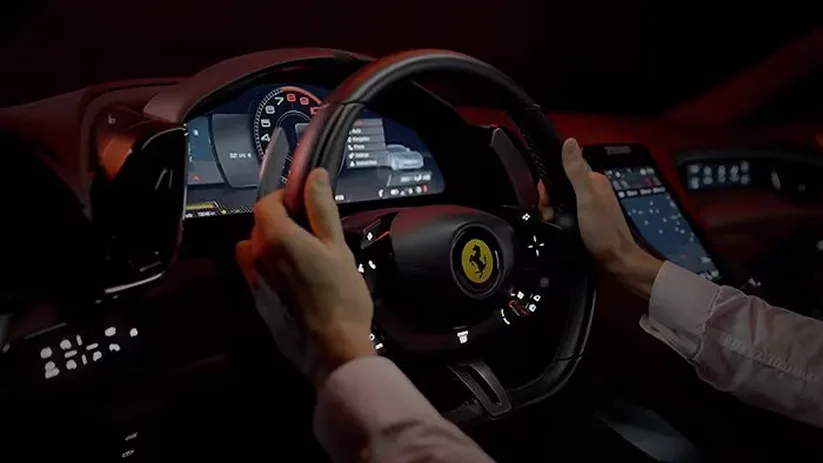 Driver's hands on a Ferrari Roma steering wheel with the passenger display lit alongside