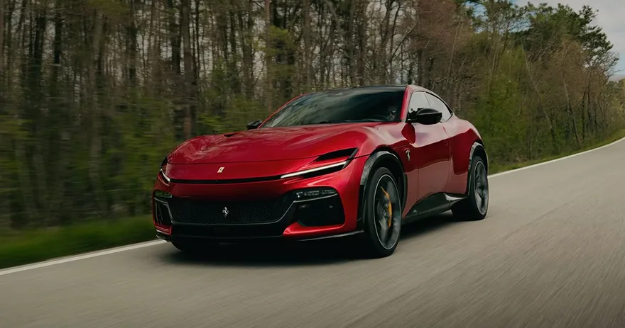 Red Ferrari Purosangue four-door driving at speed along a tree-lined country road