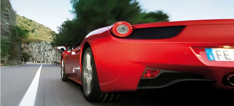 Rear view of a red Ferrari 458 Spider driving away along a sunlit hillside road