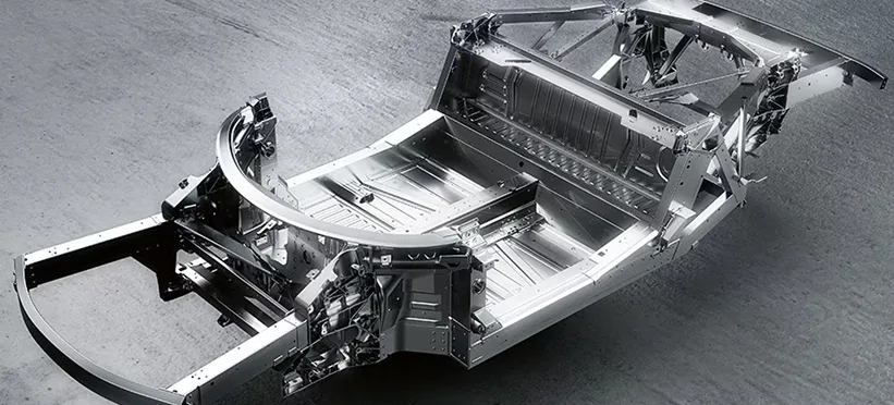 Bare aluminium spaceframe chassis of a Ferrari 458 Spider on a dark studio floor