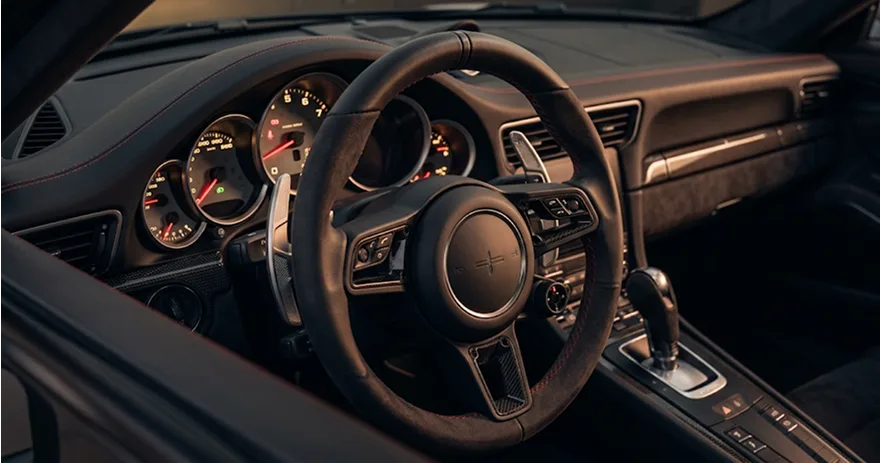 Close-up of a leather-wrapped sports car steering wheel and analogue gauge cluster
