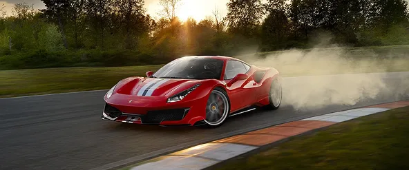 Red Ferrari 488 Pista drifting through a sunlit corner in a cloud of tyre smoke